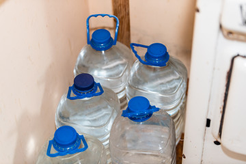 Closeup of many plastic jugs gallons filled with water and blue color caps and handles by kitchen...