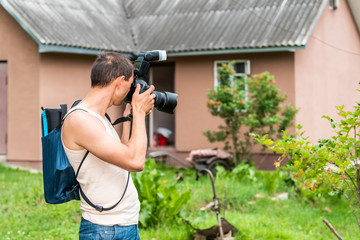 Young man photographer in garden taking picture photo of plants and house cottage real estate in...