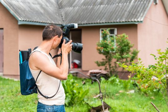 Young man photographer in garden taking picture photo of plants and house cottage real estate in green summer in Ukraine dacha