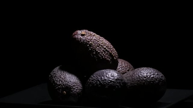 Mountain of ripe hass avocados fruit gyrating at black background