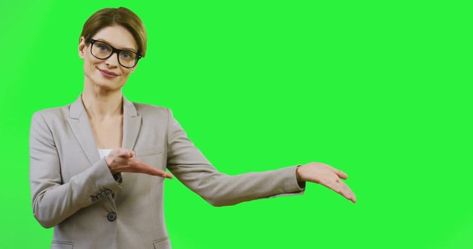 Portrait of the attractive Caucasian woman in glasses and business style demonstrating something and pointing with hands at the place where can be your logo or goods. Chroma key.