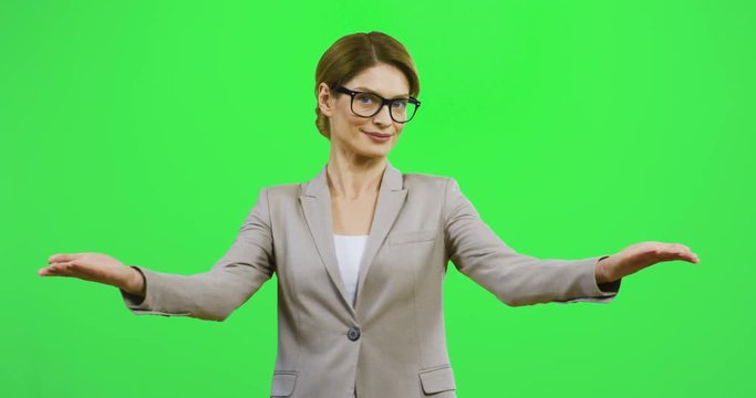Portrait of the pretty Caucasian smiled businesswoman in glasses doing a gesture with hands like advertising something, presentating and demonstrating on the chroma key background.