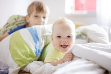 Baby girl and older brother playing on bed at home. Siblings having fun together.