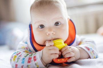 Cute baby eating fruit in nibbler on bed at home