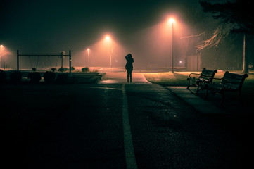 Figure stands at end of foggy path lit by streetlights. © Thomas
