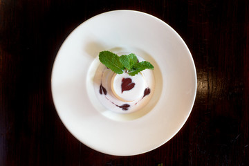 Top view Panna cotta with topping and  decorate with mint leaf and raspberry sauce serve on big white ceramic plate.