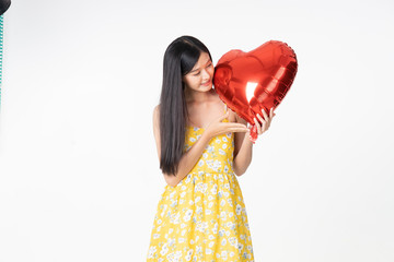 Asian young woman in yellow dress hold  red balloon heart. Young woman holding it with  being excited and surprised  holiday present isolated white  background.concept love surprise valentine day.