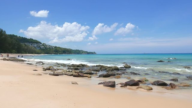 Sunny Cleanbeach With Rocks Blue Sky And Calm Ocean With Far Away Resort On Coastal Cliff And Random Far Away Silhouettes Of Tourists On Beach, Locked Shot