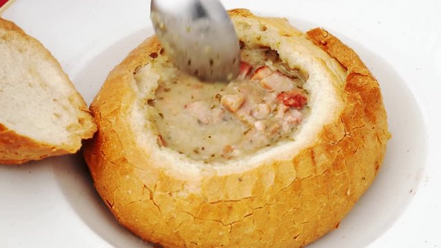 Food concept - Spoon recruit soup. Pouring polish traditional soup called zur or white borscht into bread bowl.