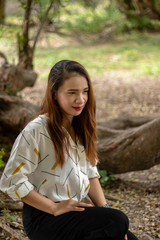 Women white skin lovely brown hair red lip wear white shirt wearing black pants women sit poses photography portrait under the tree In the garden.
