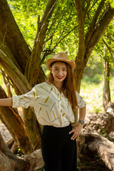 Women white skin lovely brown hair wearing a basketry hat brown red lip wear white shirt wearing black pants women standing poses photography portrait under the tree In the garden.