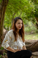 Women white skin lovely brown hair red lip wear white shirt wearing black pants women sit poses photography portrait under the tree In the garden.