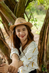 Women white skin lovely brown hair wearing a basketry hat brown red lip wear white shirt wearing black pants women sit poses photography portrait under the tree In the garden.