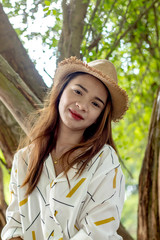 Women white skin lovely brown hair wearing a basketry hat brown red lip wear white shirt wearing black pants women sit poses photography portrait under the tree In the garden.