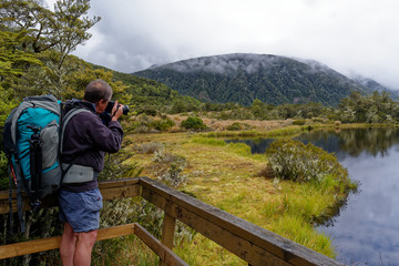 Fototapeta na wymiar The photographer being photographed taking a photo of the small lake at the Alpine Nature Walk, in Lewis Pass, New Zealand