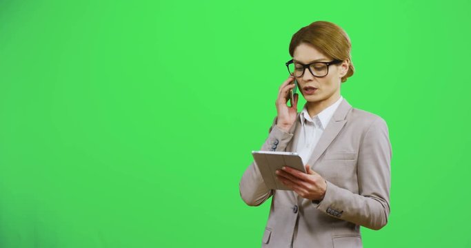 Caucasian business lady in glasses having a talk on the phone about her business and looking at the tablet device in her gands. Chroma key. Alpha channel.