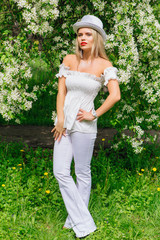 Sexy modern bride in white cylinder hat enjoing bloomin apple tree flowers.