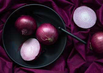 A whole red onion and a cut red onion in a bowl.