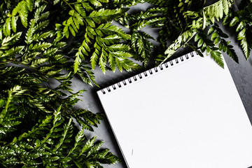 Notebook and green leaves lying on gray background. Flat lay, top view. Place for text