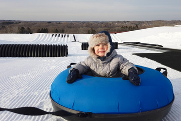 Tubing in Snow park, winter activities.  Kid is looking at camera and smiling