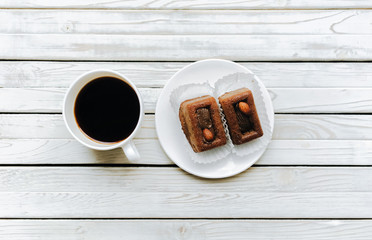 Two muffins with almond on white dish near cup of coffee on grey wooden background. Top view.