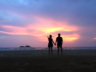 Couple hold each other hand at the beach under sunset. What a perfect moment under the sunset sky!