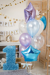 Birthday blue and purple decorations with gifts, toys, garlands and figure for little baby party on a white bricks background.
