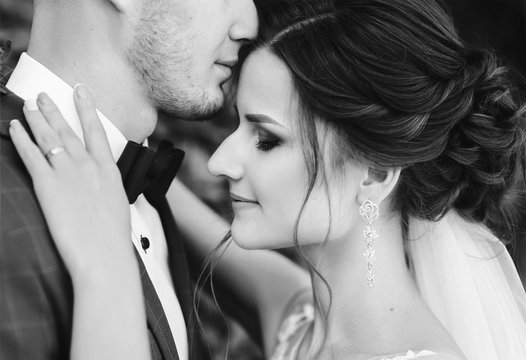 Beautiful newlyweds hugging and smiling on trees background. Young bride and cute bride close-up. Wedding black and white, monochrome photography. Stylish portrait.