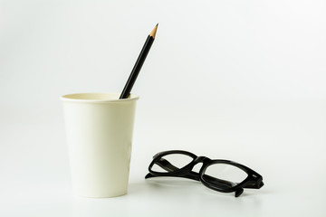 pencil in a paper coffee cup and eyeglasses on white background.