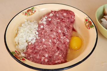 fresh beef and pork minced meat sprinkled with white onions and chicken egg for making cutlets and schnitzel in a yellow iron plate. meat patties