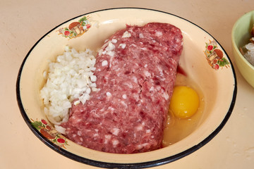 fresh beef and pork minced meat sprinkled with white onions and chicken egg for making cutlets and schnitzel in a yellow iron plate. meat patties. On the kitchen table.