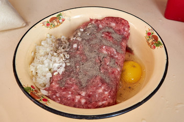 fresh beef and pork minced meat sprinkled with white onions and chicken egg and pepper for making cutlets and schnitzel in a yellow iron plate. meat patties