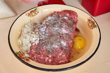 fresh beef and pork minced meat sprinkled with white onions and chicken egg and salt and pepper for making cutlets and schnitzel in a yellow iron plate. meat patties