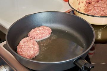at home in the kitchen is fried in a hot pan on an electric stove of minced meat pork and beef patties