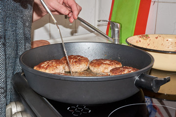 female chef at home in the kitchen frying on a hot pan on an electric stove meatballs pork and beef. minced meat patties