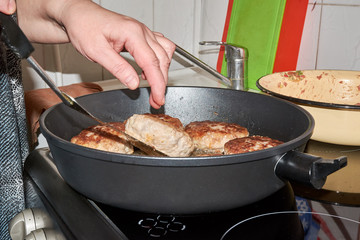woman chef fries meat cutlets in a pan turning them over with a hand and spatula for cooking