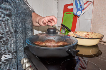 a frying pan on an electric stove with a closed lid at home in the kitchen. woman opens the frying pan lid with steam