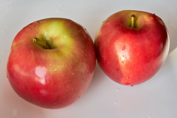 Two red apples lie on a white plate.