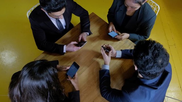 Handheld top angle shot of four colleagues on a cafe table occupied with their smart portable technology device, one of them tries to get attention of the others but fails in desperation 
