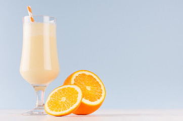 Bright oranges milkshake with slices citrus, striped straw on white wooden table and pastel light blue wall.