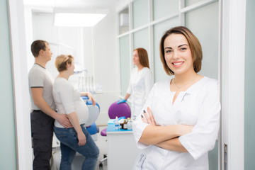Fototapeta premium Young beautiful woman doctor stands against the background of patients in the clinic. Patients married couple, woman pregnant