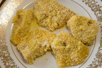 Breaded meat on a plate in corn breadcrumbs.