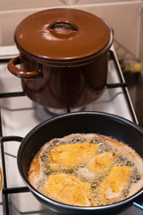 Frying cutlets in a pan on a plate with a brown pot in the background.