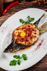 The concept of Georgian cuisine. Baked fish Mackerel Adzhar. Serving dishes in Georgian restaurant on a white plate, on a wooden table. Background image. copy space