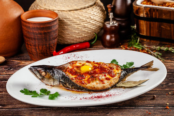 The concept of Georgian cuisine. Baked fish Mackerel Adzhar. Serving dishes in Georgian restaurant on a white plate, on a wooden table. Background image. copy space
