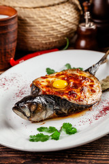 The concept of Georgian cuisine. Baked fish Mackerel Adzhar. Serving dishes in Georgian restaurant on a white plate, on a wooden table. Background image. copy space