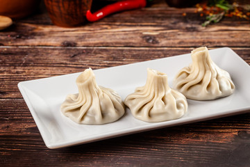 The concept of Georgian cuisine. Khinkali from white dough with meat. Serving dishes in Georgian restaurant on a white plate, on a wooden table. Background image. copy space