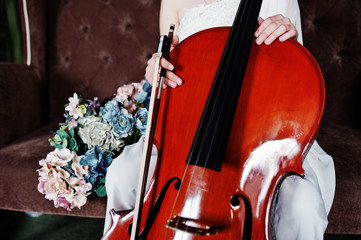 Close up of gilrl musician in white dress with double bass sitting on brown vintage sofa.