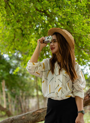 Women tourists women white skin lovely brown hair wearing a basketry hat wear white shirt wearing black pants in hand have a camera traipse photograph nature.