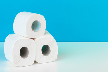 Three toilet paper rolls isolated on white table with blue background